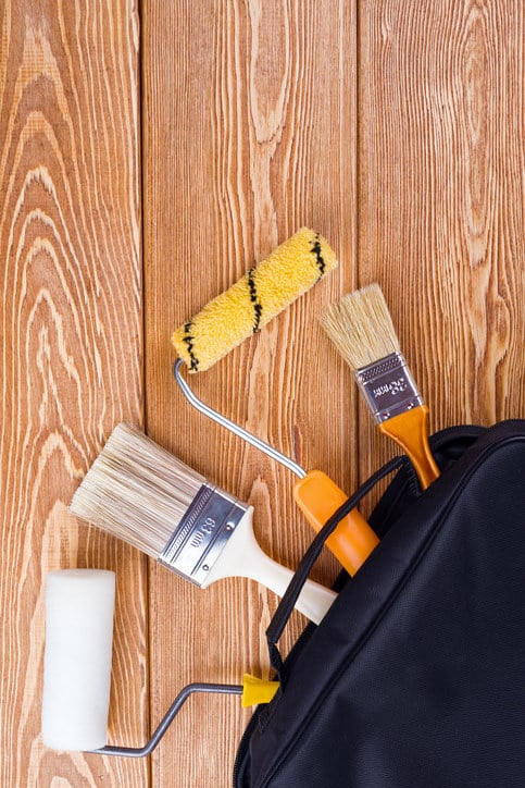 Outils professionnels de peinture en bâtiment à moitié sortis de leur étui de rangement posé sur des planches en bois