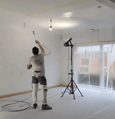 Peintre appliquant de la peinture avec un pulvérisateur à l'intérieur d'une nouvelle construction