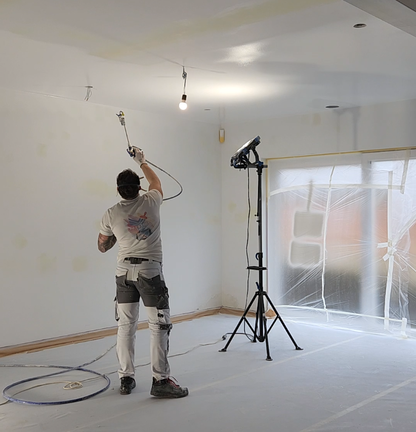 Peintre appliquant de la peinture avec un pulvérisateur à l'intérieur d'une nouvelle construction