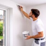 Peintre professionnel réalisant une finition de peinture intérieure sur l’angle mur-plafond à Arlon